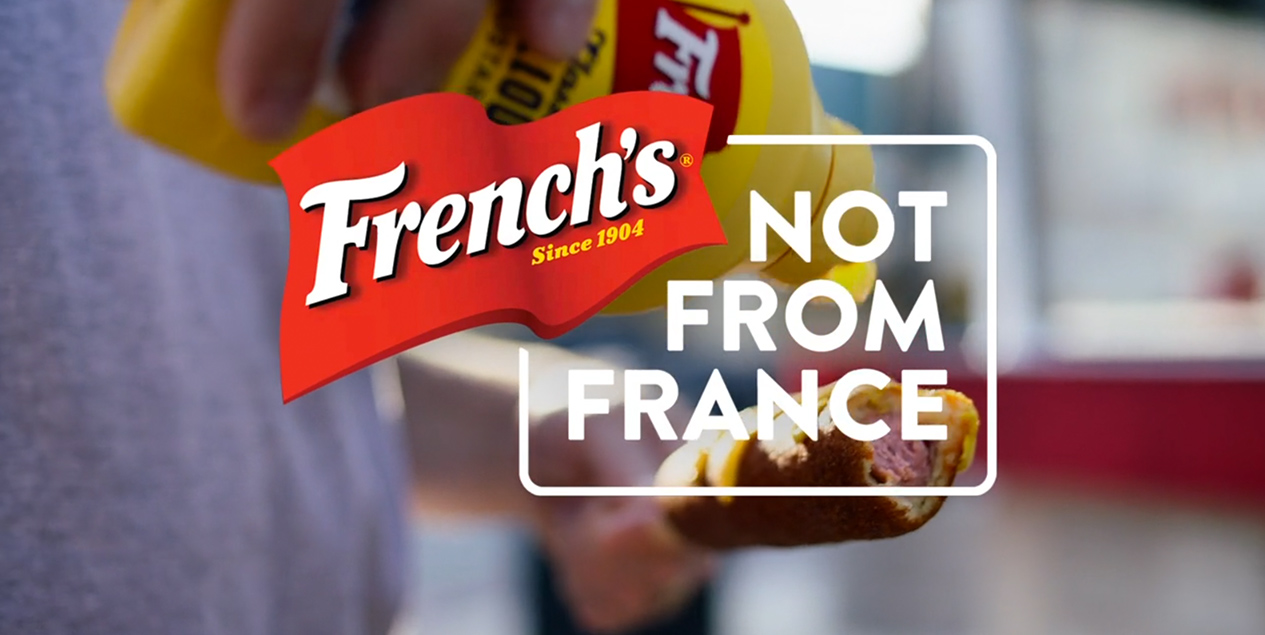 Man putting mustard on hotdog behind French's logo